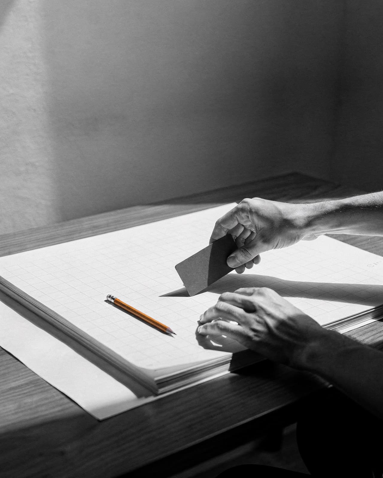 Dłonie układające czarną kartę komponentu na papierze z siatką — still life ze studia projektowego